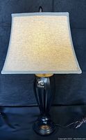 Full view of the Ashley Design Signature table lamp showing beige fabric shade and black metal base on a black background.
