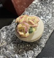 Close-up of the top of a porcelain lidded box showing detailed cream and pink flower cluster on lid.