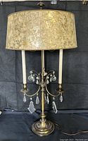 Full view of the vintage Stiffel bouillotte table lamp showing brass base, three arms with crystal pendants, and original large cream and gold tortoiseshell patterned lamp shade.