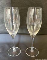 Two clear Riedel wine glasses side by side on a gray surface showing overall shape and condition.