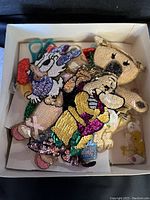 Box containing a collection of colorful handmade sequin patches featuring Disney characters and various animals, including a small pair of scissors and a small doll patch.