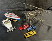 Overall collection of vintage toys including a metal wireframe biplane sculpture, tin litho speedboat, and three die-cast cars.
