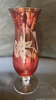 Front view of cranberry etched floral hurricane glass footed vase on footed base with flared rim.