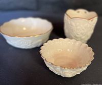 Front angled photo showing ivory colored Lenox votive holder with rose design and two matching Lenox tea rose bowls with 24kt gold trim on scalloped edges.