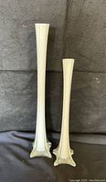 Full view of two white hand-blown glass bud vases shaped like the Eiffel Tower, one taller than the other.