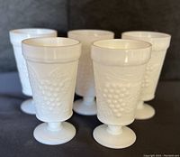 Front and slightly angled view of all five milk glass water glasses grouped together, showcasing the grapevine relief design and thick glass construction.