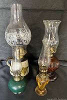 Full view of all four vintage oil lamps showing different colors and glass chimneys of varying shapes and sizes.