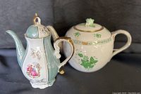 Two porcelain teapots displayed against a black background, showing full side views including handles and spouts