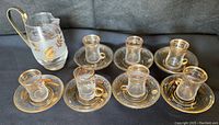 Set of seven vintage Turkish tea glasses with matching saucers and a small Libbey pitcher, all with gold leaf and frosted glass details.