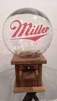 Front view of vintage gumball or peanut machine with clear glass globe showing Miller logo in red and High Life text in yellow.