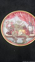 Full view of circular metal tray with painted still life of fruit, flowers, and an ornate pitcher framed by red curtains and yellow edge border.