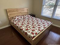 Queen size wooden bed with floral mattress placed in bedroom near window and nightstand.