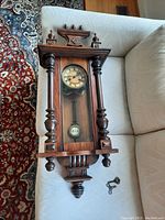 Front view of wooden antique wall clock laid on sofa with winding key displayed