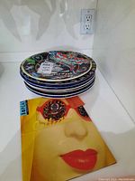 Stack of six 10-inch plates and one smaller plate next to BOPLA Switzerland brochure