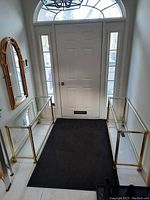 Two brass-framed console tables placed in an entryway, one on each side of a white door with sidelights.