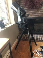 Assembled Celestron telescope on tripod with motorized mount beside fireplace