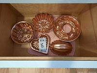 Top down photo of all five copper bakeware molds inside a drawer on a pink cloth.