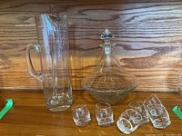 Crystal pitcher with handle, decanter with stopper, and six tumbling shot glasses displayed.