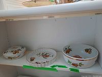Full set of three pieces displayed on shelf, showing covered serving dish, pie dish and salad bowl with fruit designs and gold trim