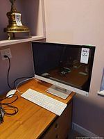 Front view of silver all-in-one desktop on stand with screen off, keyboard and mouse on desk