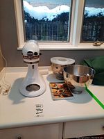 Front view of white KitchenAid stand mixer head and base with two stainless bowls and recipe book