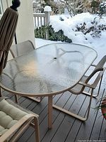 Patio table with textured glass top and metal frame, four chairs, umbrella and stand seen on a covered porch with snow outside.