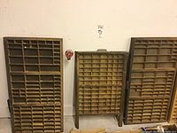 Three antique wooden printer's trays arranged standing up against a white wall in a garage setting.