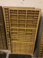 Two wooden antique printers trays standing upright against a wall, showing all compartment sections.