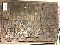 Wide view of the wooden tray filled with various wooden printers type blocks showing letters, numbers, and symbols arranged tightly in a grid pattern.