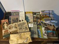 Overview shot of vintage ephemera including postcards, booklets, canvas pouch, and photograph reproductions laid on table