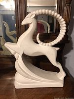 Side view of white textured ibex figurine placed on wooden table in front of mirror.