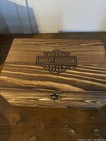Closed wooden box with top surface showing burnt Harley-Davidson Motor Cycles logo.
