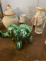 Green metallic balloon dog figurine displayed on wooden table alongside ceramic and glassware pieces