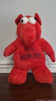 Front view of red plush toy with 'Hostess MUNCHIES' embroidered on chest, standing on flat surface.