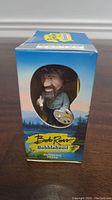 Boxed bobblehead figure of Bob Ross with visible window showing the figure inside and colorful packaging design.