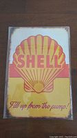 Photo of a rectangular metal advertising sign with Shell logo and slogan