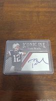 Front view of Tom Brady trading card in protective case showing printed image, facsimile autograph, and branding.