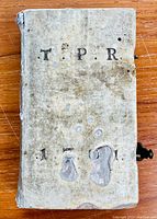Front cover of vellum-bound book showing wear, discoloration, and letters T.P.R. and I.O.I.