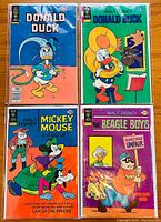 Four vintage Walt Disney comic books laid out on a wooden surface showing front covers of Donald Duck, Mickey Mouse & Goofy, and The Beagle Boys.