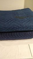 Two stacked blue moving pads with quilted stitching and visible wear marks on top. The focus is on the condition and material of the blankets.