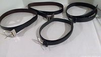 Four black leather belts laid out in a circle, showing different buckle styles and sizes 34 and 36.