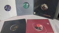 Five 12-inch vinyl records in different colored sleeves arranged on a surface.