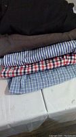 Stack of five men's shirts in black, gray, and various checkered and striped patterns.