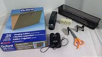 Box containing 25 Oxford letter size hanging folders with various office supplies including stapler, power strip, scissors, tape dispenser, pen holders, and metal mesh desk organizer.