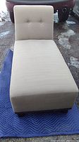 Full view of khaki/tan lounge chair with cushioned backrest and seat, two buttons on backrest, placed on a blue quilted mat outdoors