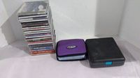 Stack of CDs in jewel cases next to two CD holders, one purple, one black.