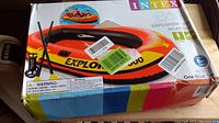 Box showing Intex Explorer 300 inflatable boat set with graphics and included pump and oars, visible wear and damage on box corners.