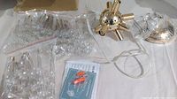 Photo showing multiple small bags of hanging crystal-like pieces, instruction sheet, wiring, and central gold sputnik chandelier body with several arm sockets.