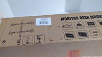 Photo showing box front with illustration of quad monitor mount system and key specs including monitor compatibility (13" to 32"), weight rating, VESA compatibility, and rotation/tilt details.
