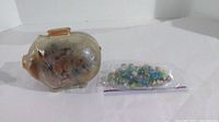 Photo of glass piggy bank filled with pennies and bag of marbles placed beside it, showing size and contents.